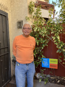 Elderly man, Manuel, standing in front of his door smiling.