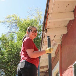 Young girl on latter painting outside of a house.