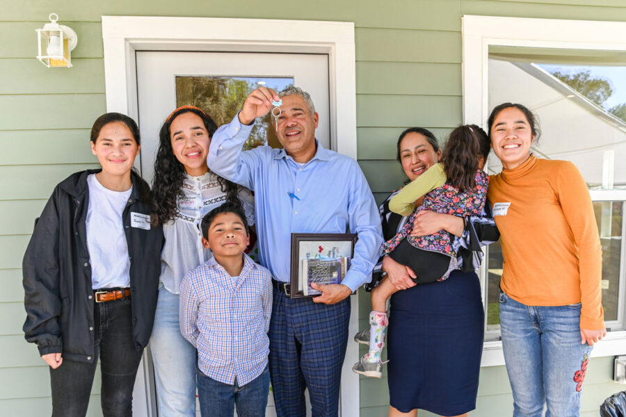 Large family standing on the poach of their new home. Father showing off the new keys.