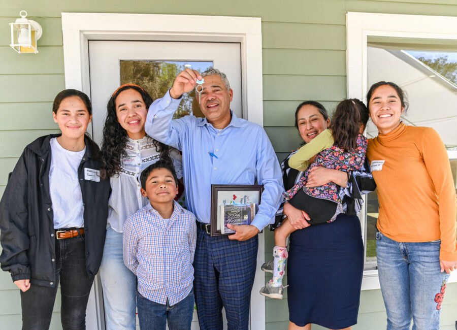 Large family standing on the poach of their new home. Father showing off the new keys.