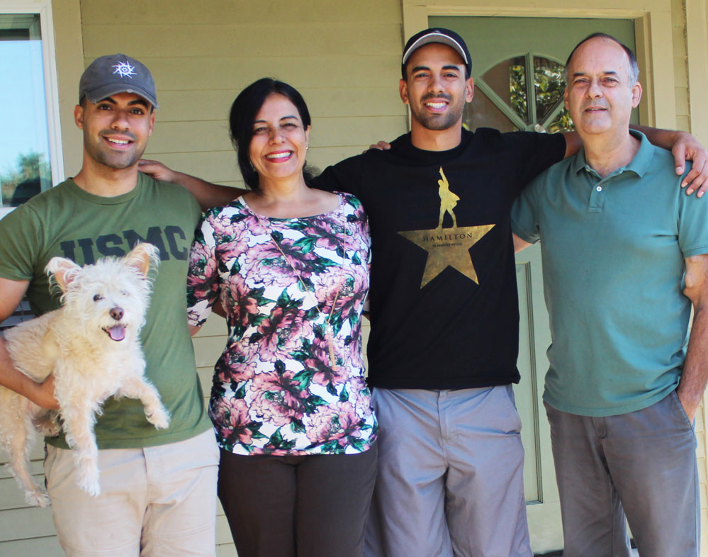 Family with dog standing on their poach with their arms around each other.