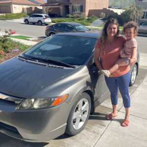 Mom hold her little daughter smiling in front of Honda Civic.