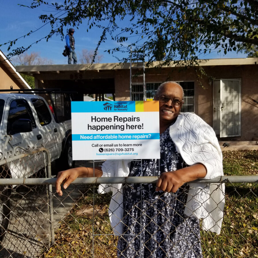 African American lady with big smile, standing in front of her house next to a Habitat for Humanity home repair sign.