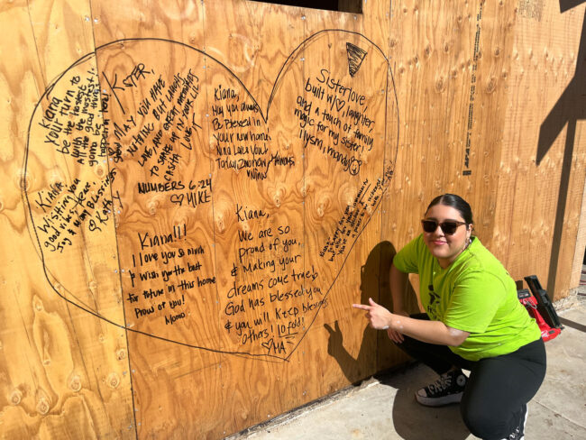 Young Lady pointing at a wooden board with messages of encouragement for Homeownership Dreams Coming True.