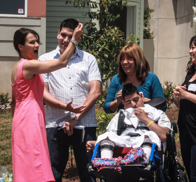 Happy Family with disabled son in wheelchair, standing front of their new home and wife holding the keys for You Can Change the Lives of 200 Families – Framing the Future.