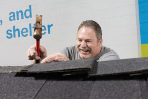 Older man hammering a nail on a roof.