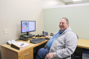 Older man sitting at a desk smiling.