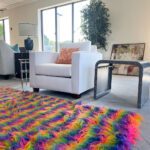 White small love seat couch in front of a rainbow fluffy carpet.