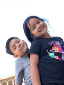 Young boy with his older sister smiling into the camera.