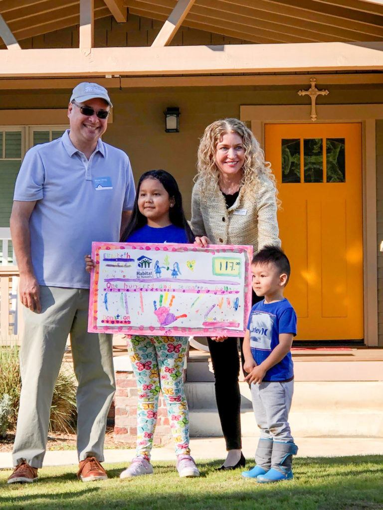 Young girl, Elizabeth, holding a sign with young boy, her brother, and two adults in front of a house.