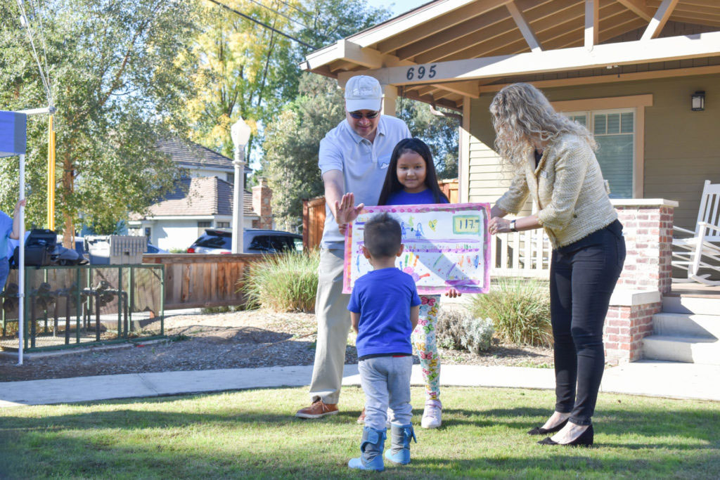 Young girl, Elizabeth, holding a sign with young boy, her brother, and two adults in front of a house.