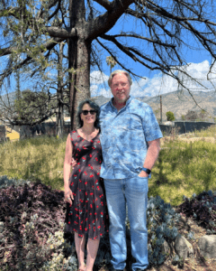 man and woman standing on a lot with grass and trees

