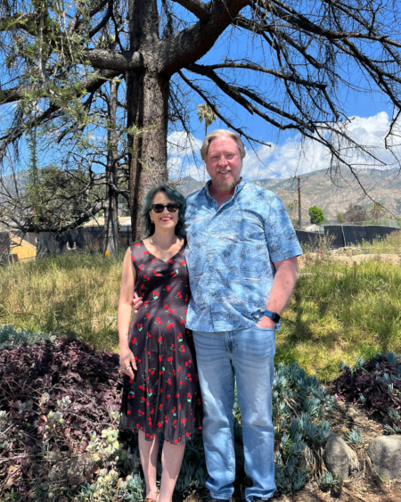 man and woman standing on a lot with grass and trees