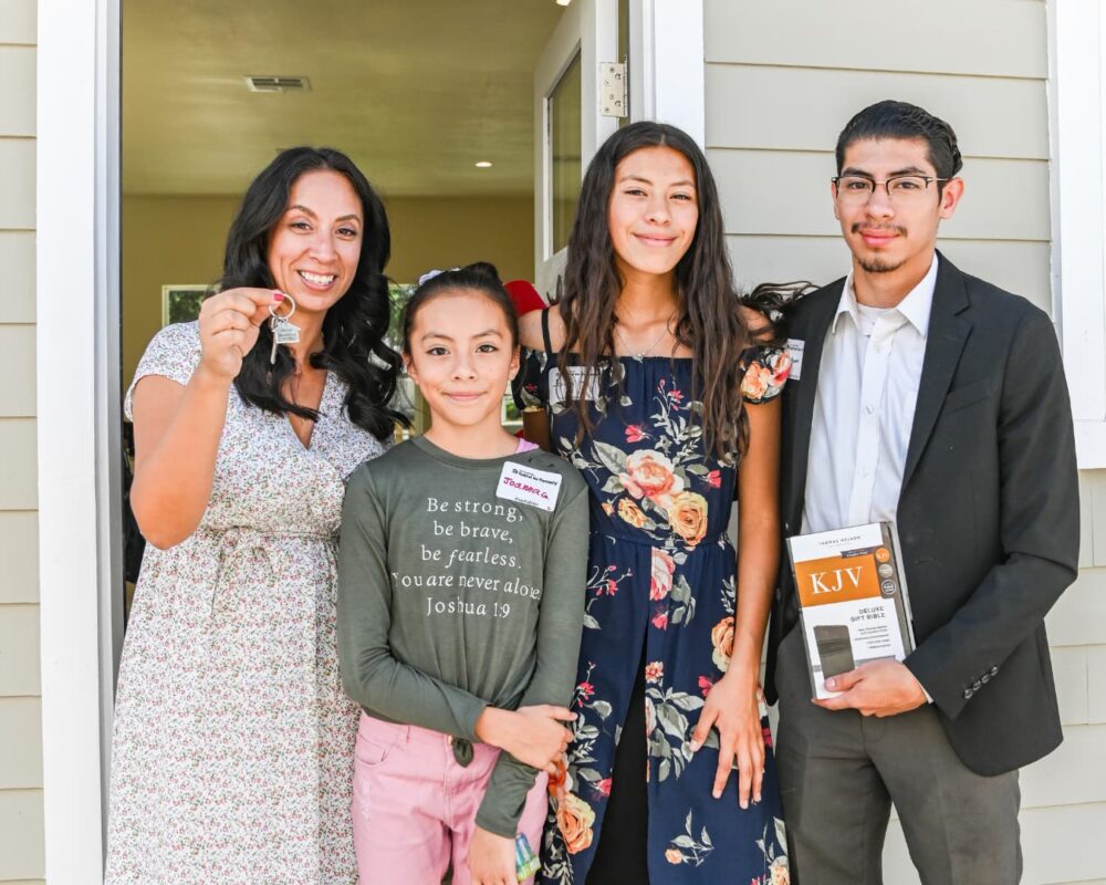 Woman smiling and holding keys, standing next to her children in front of a door