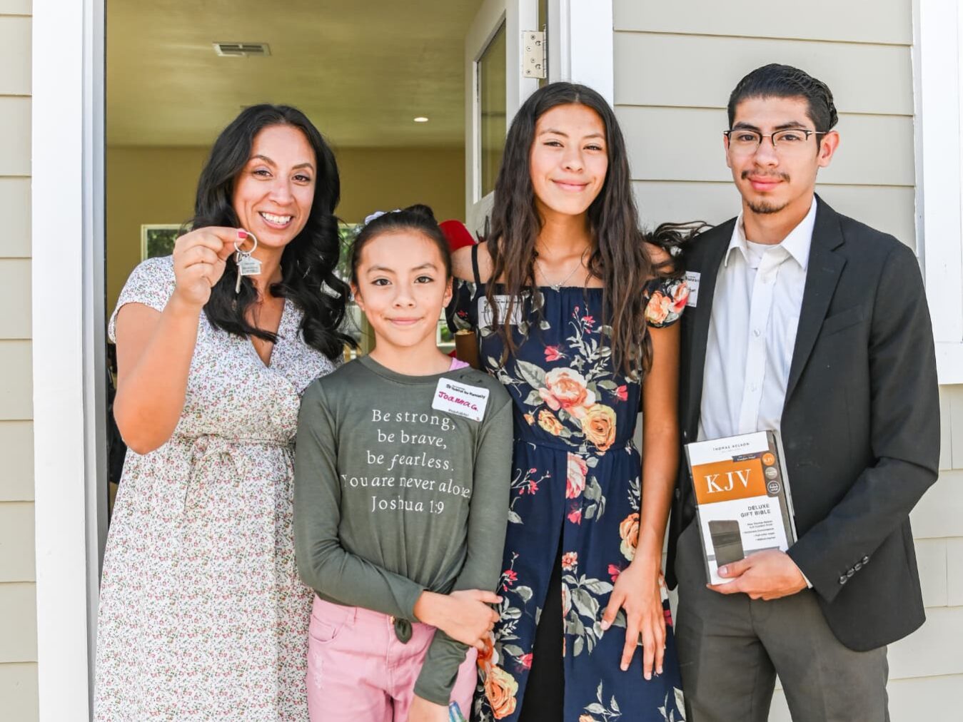 Woman smiling and holding keys, standing next to her children in front of a door