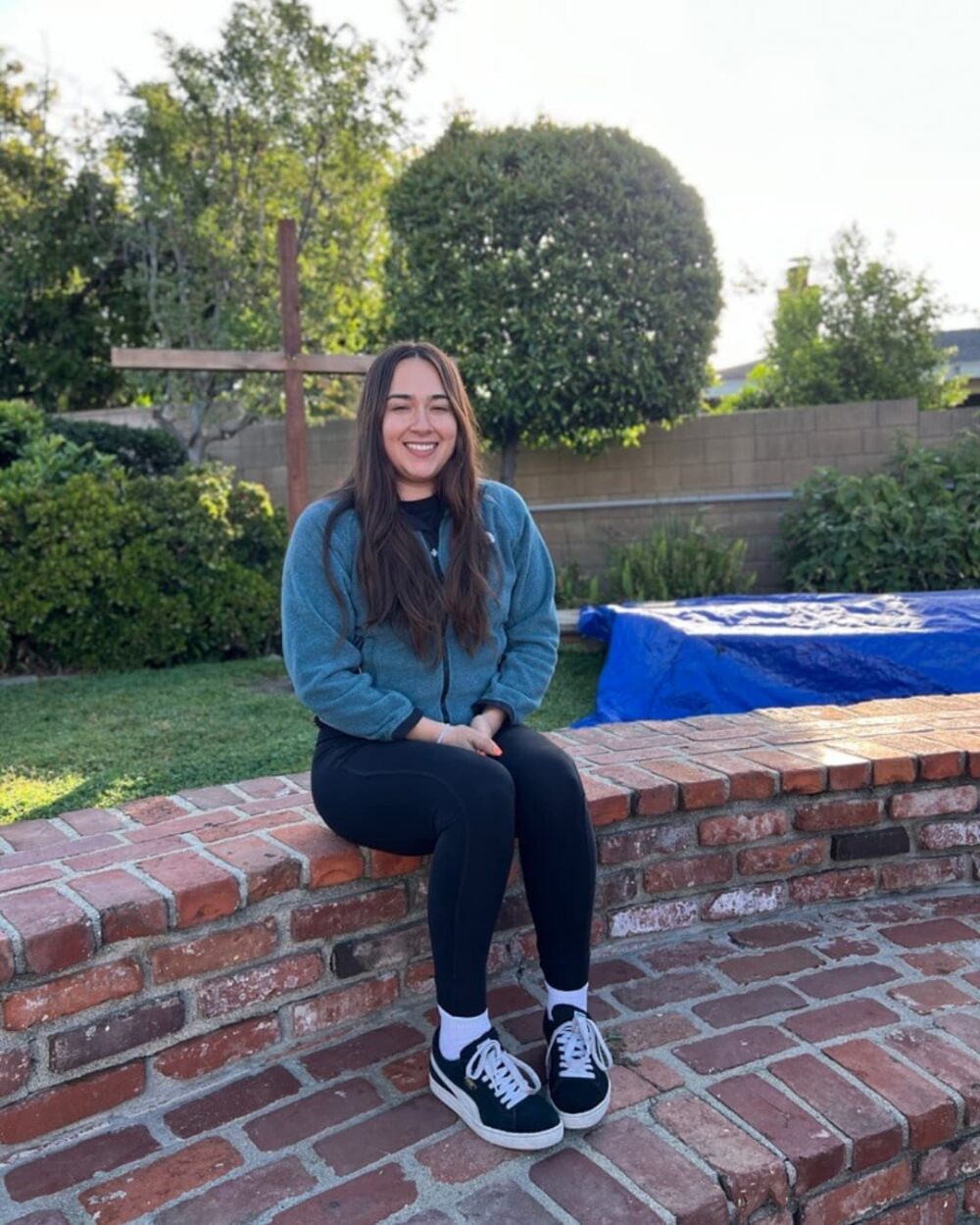 A woman sitting on a brick fence and smiling