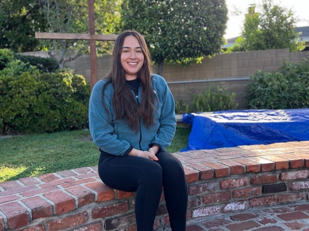 A woman sitting on a brick fence and smiling