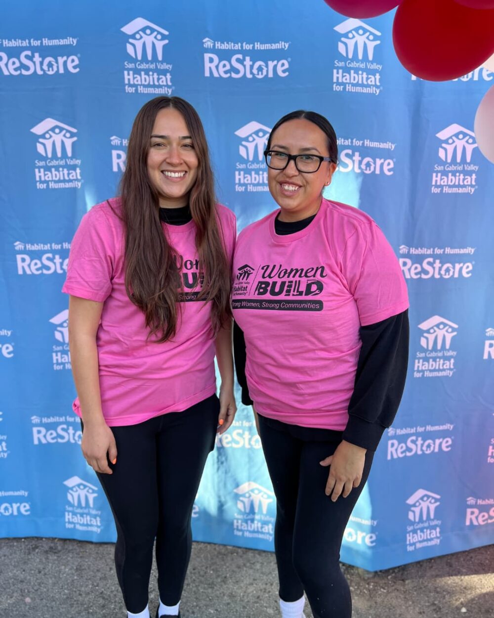Two women smiling in pink shirts, standing in front of a blue background