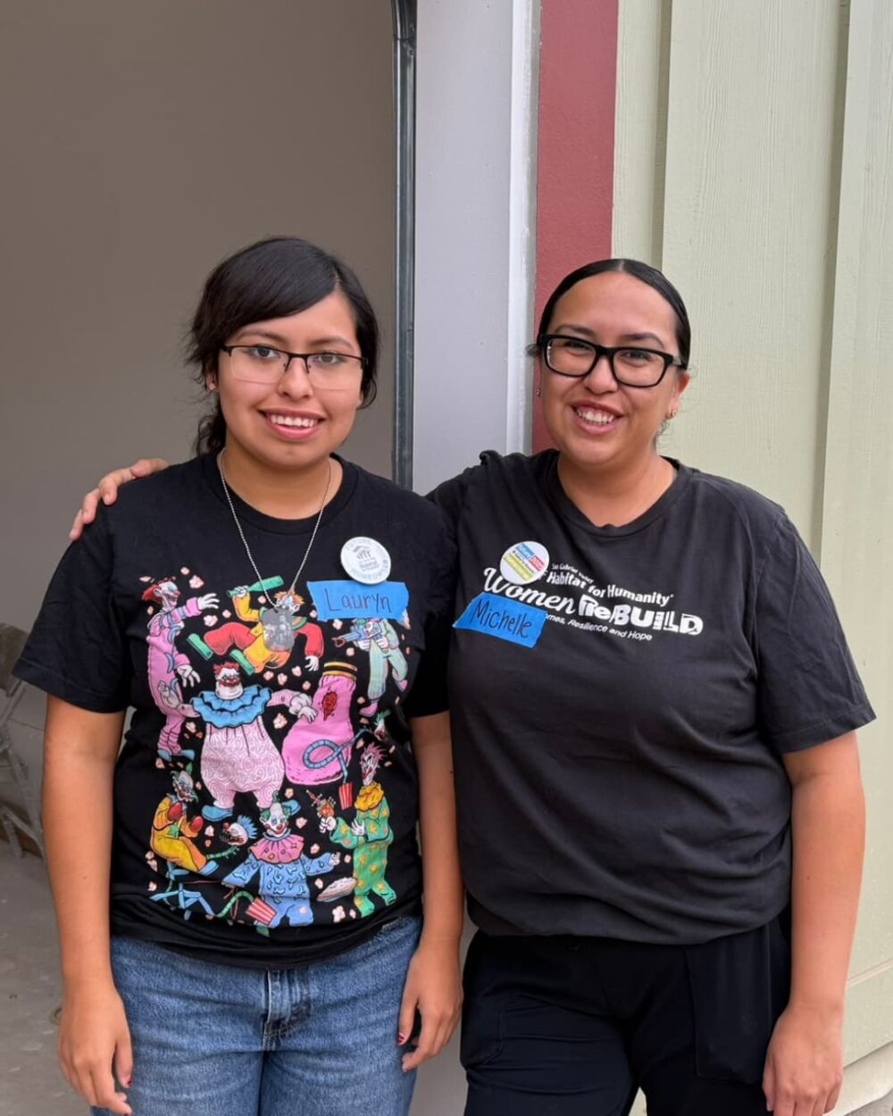 Two women standing and smiling in front of a home