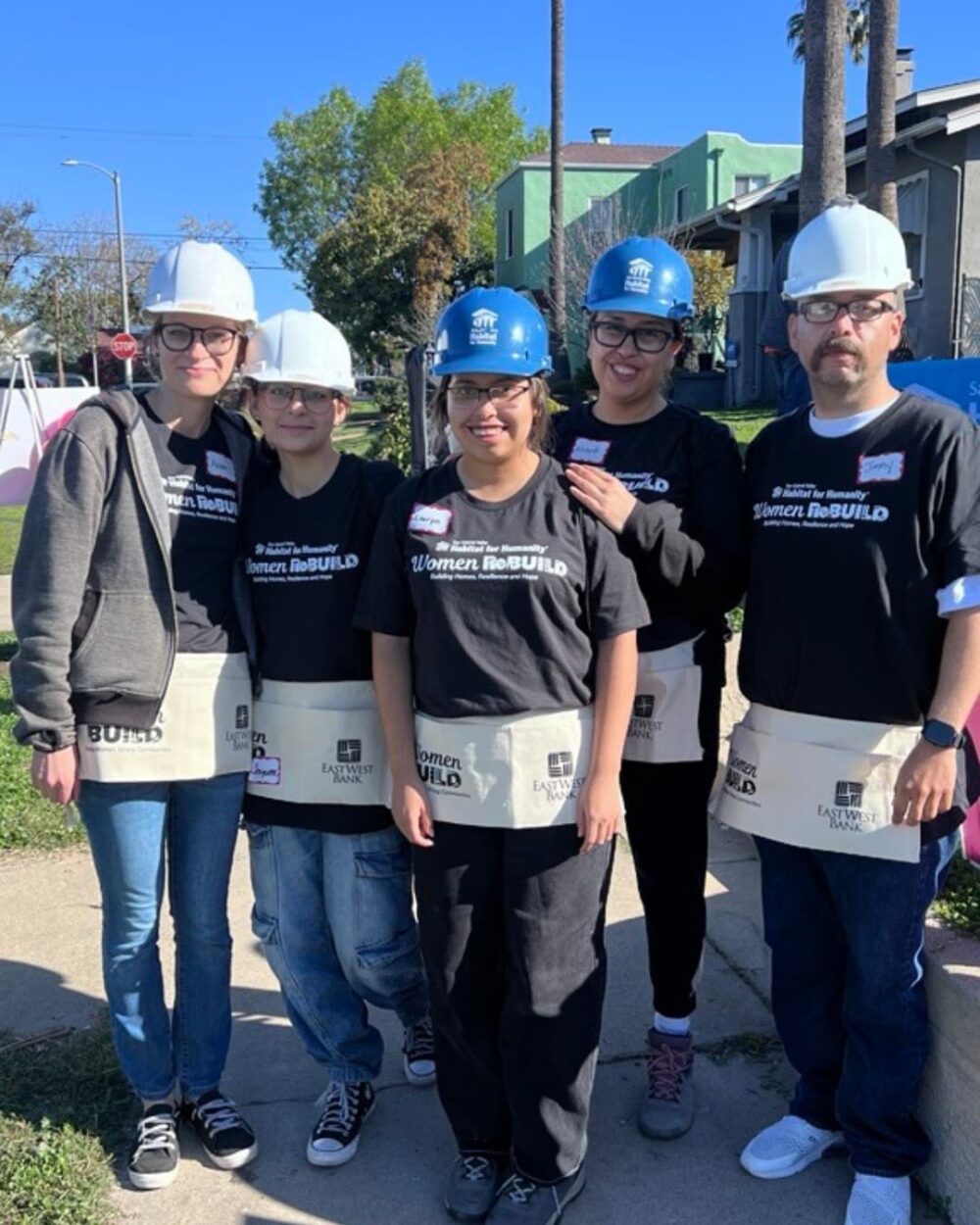 A group of five people in hardhats and black shirts standing outside and smiling