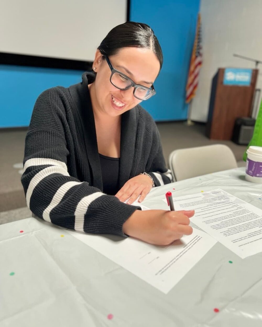 A woman smiling and signing a document while seated
